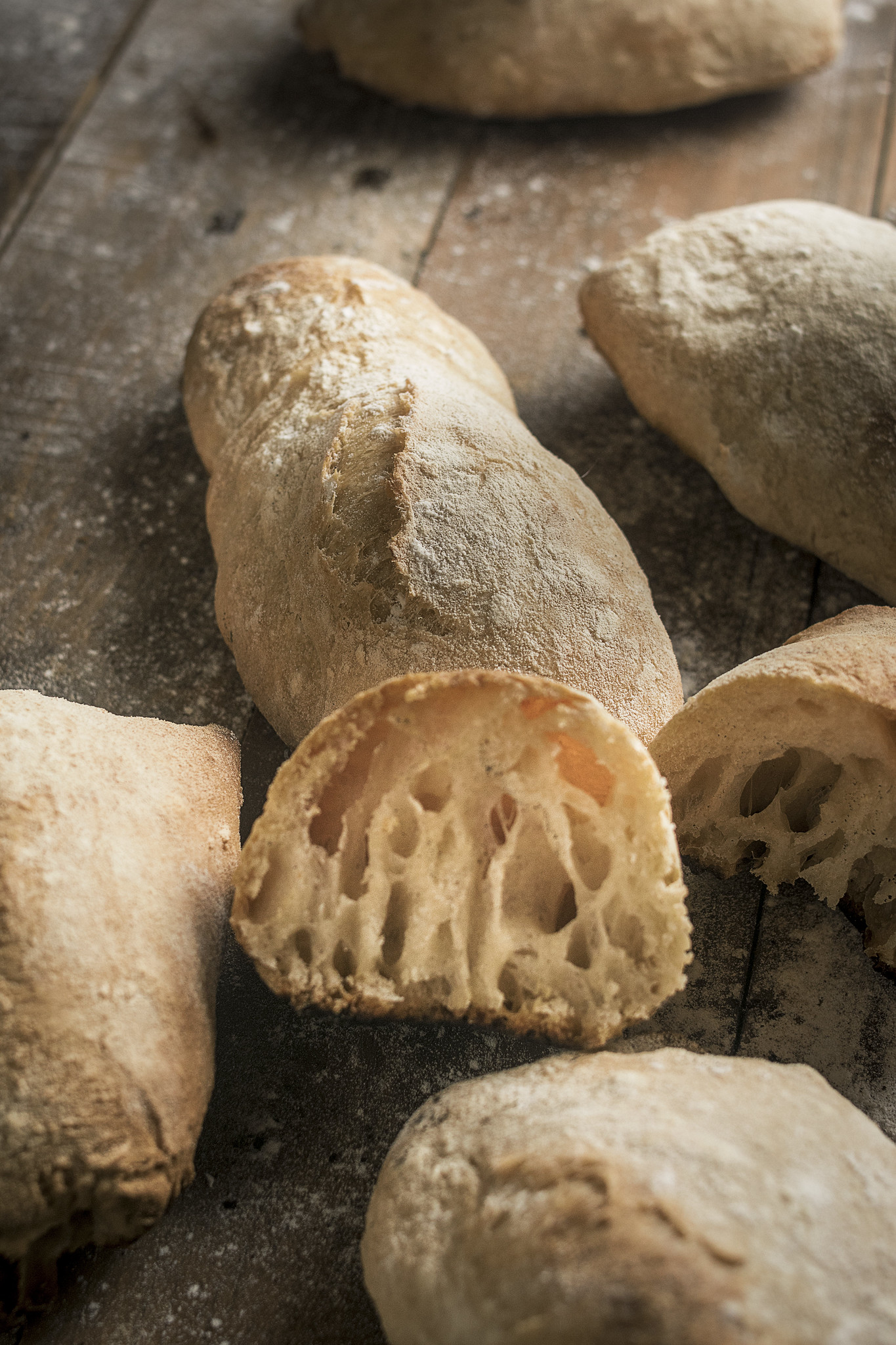 No-knead ciabatta rolls with a cut-open roll showing an airy crumb and flour-dusted crust.